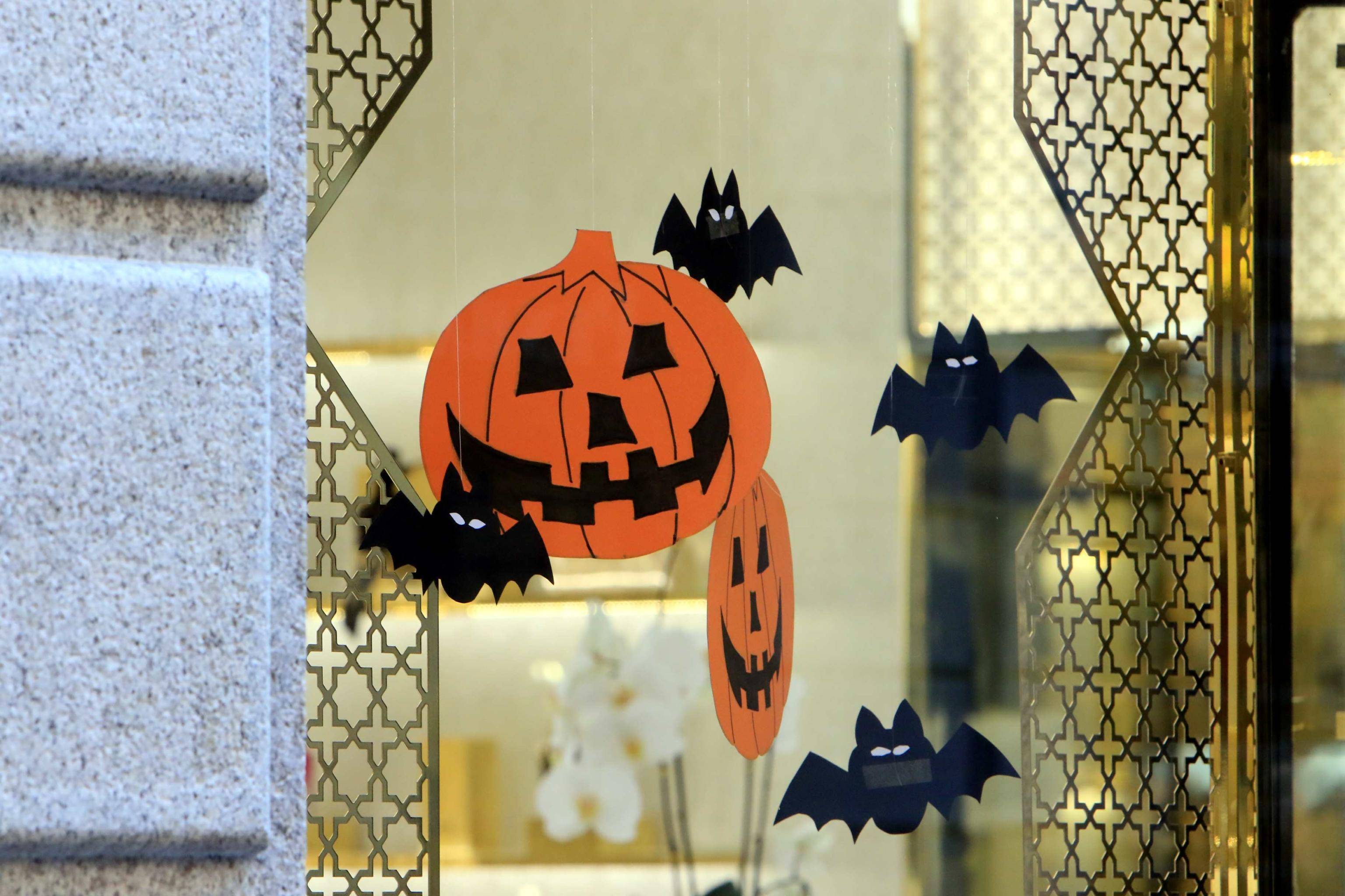 10月30日,在意大利米兰,戴口罩的行人从一个贴着万圣节装饰的商店橱窗