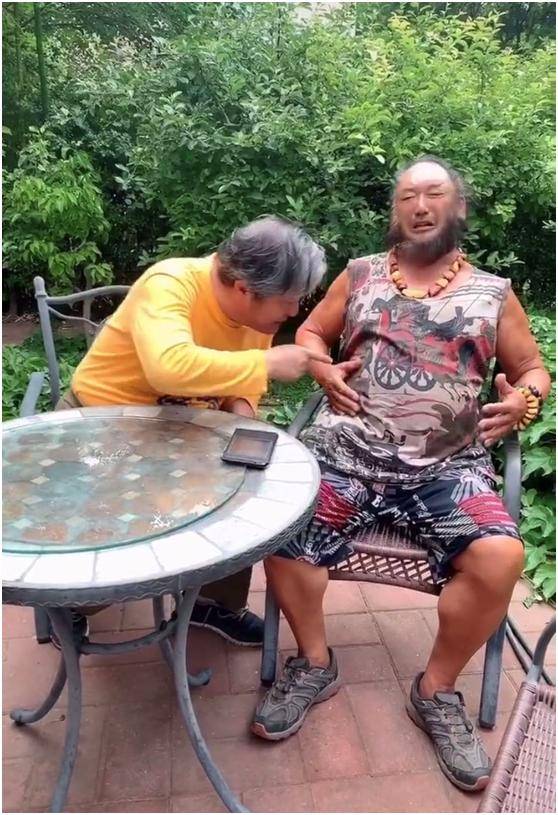 视频中,贾石头身穿花色的背心和短裤,脖子上和手腕上都戴着文玩,头发