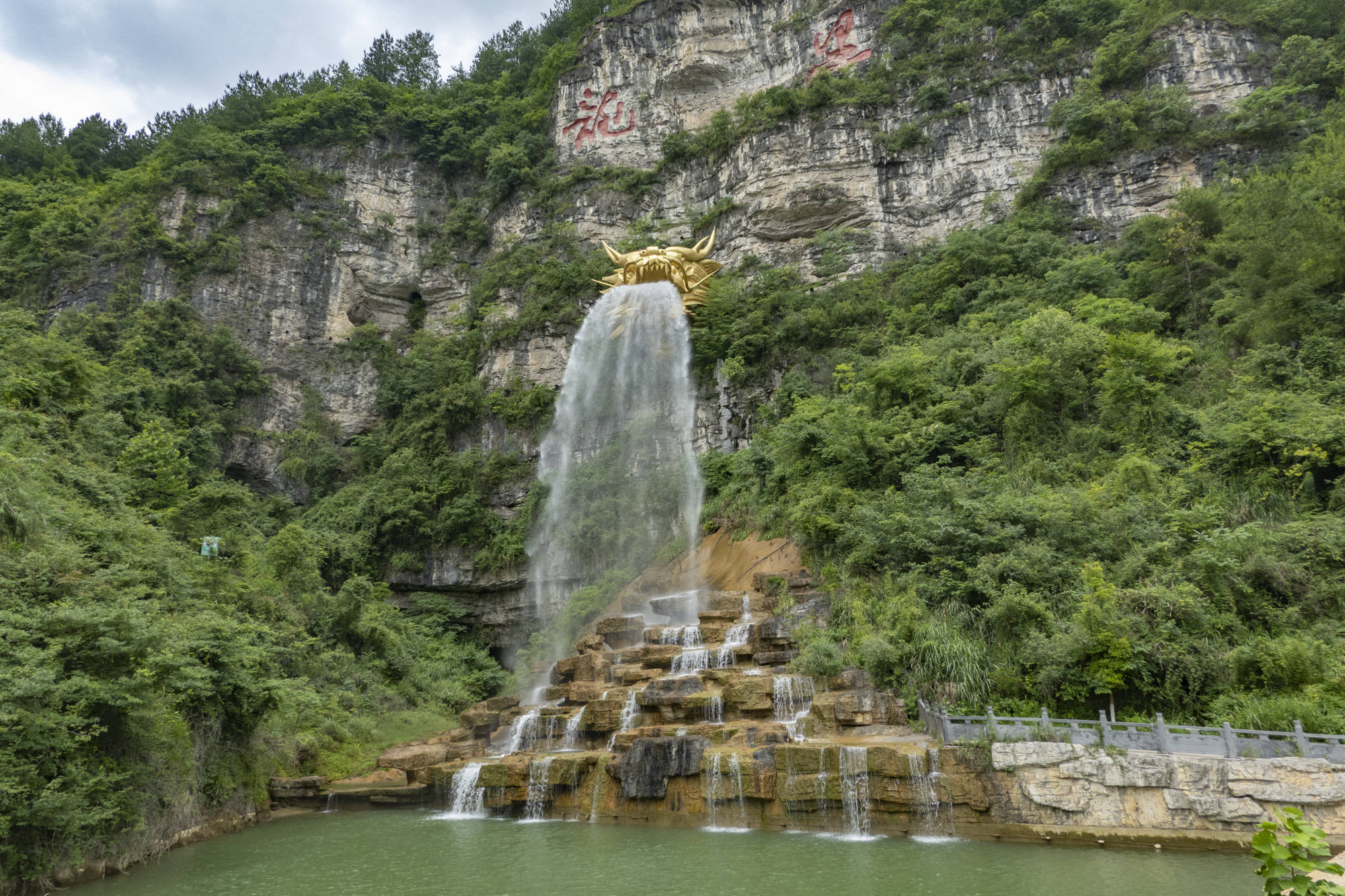 飞瀑下是一处水潭,四周巨石点缀,鲜花簇拥,许多远方游客和经过的路人