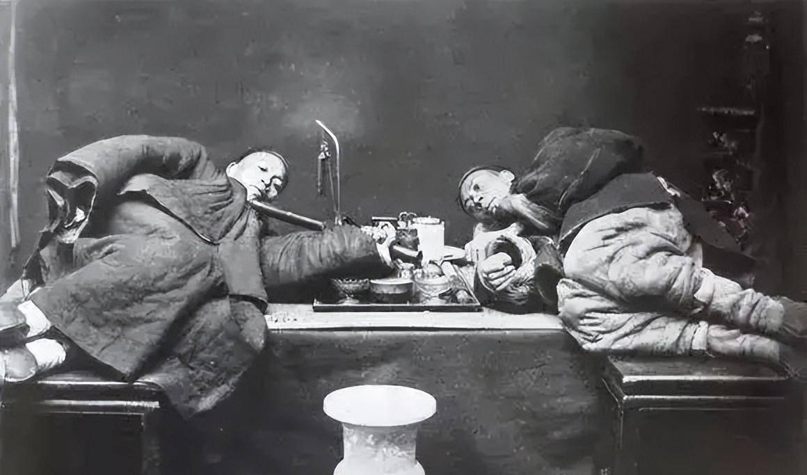 一人正在看报纸,抽着鸦片议论时局两个大烟鬼躺在烟塌上吸食大烟,一人