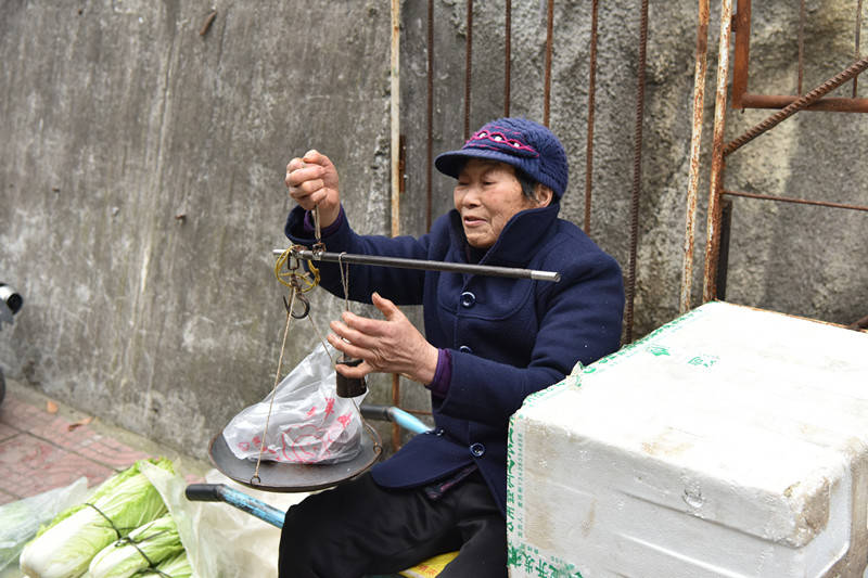 卖菜的老人还在使用杆秤为了节省木炭,摆摊的几个老人围着一个火笼