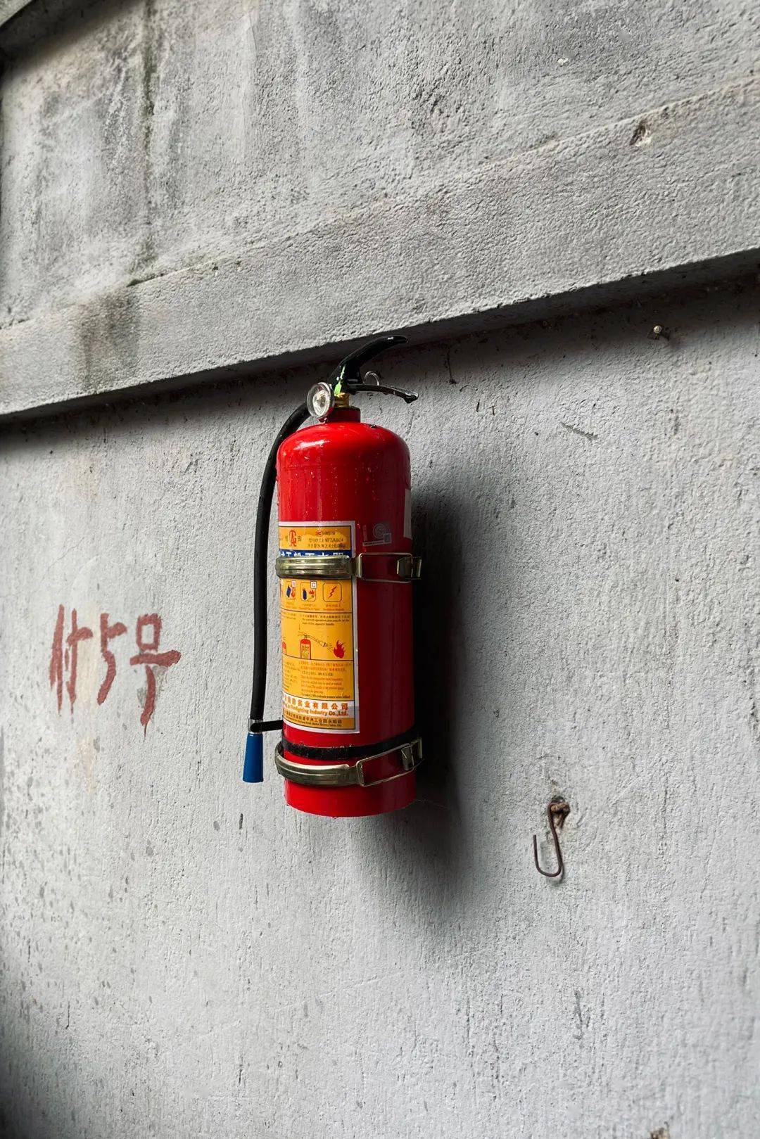 在黎黄陂路黄陂村居民区的墙上,挂着一瓶手提式干粉灭火器