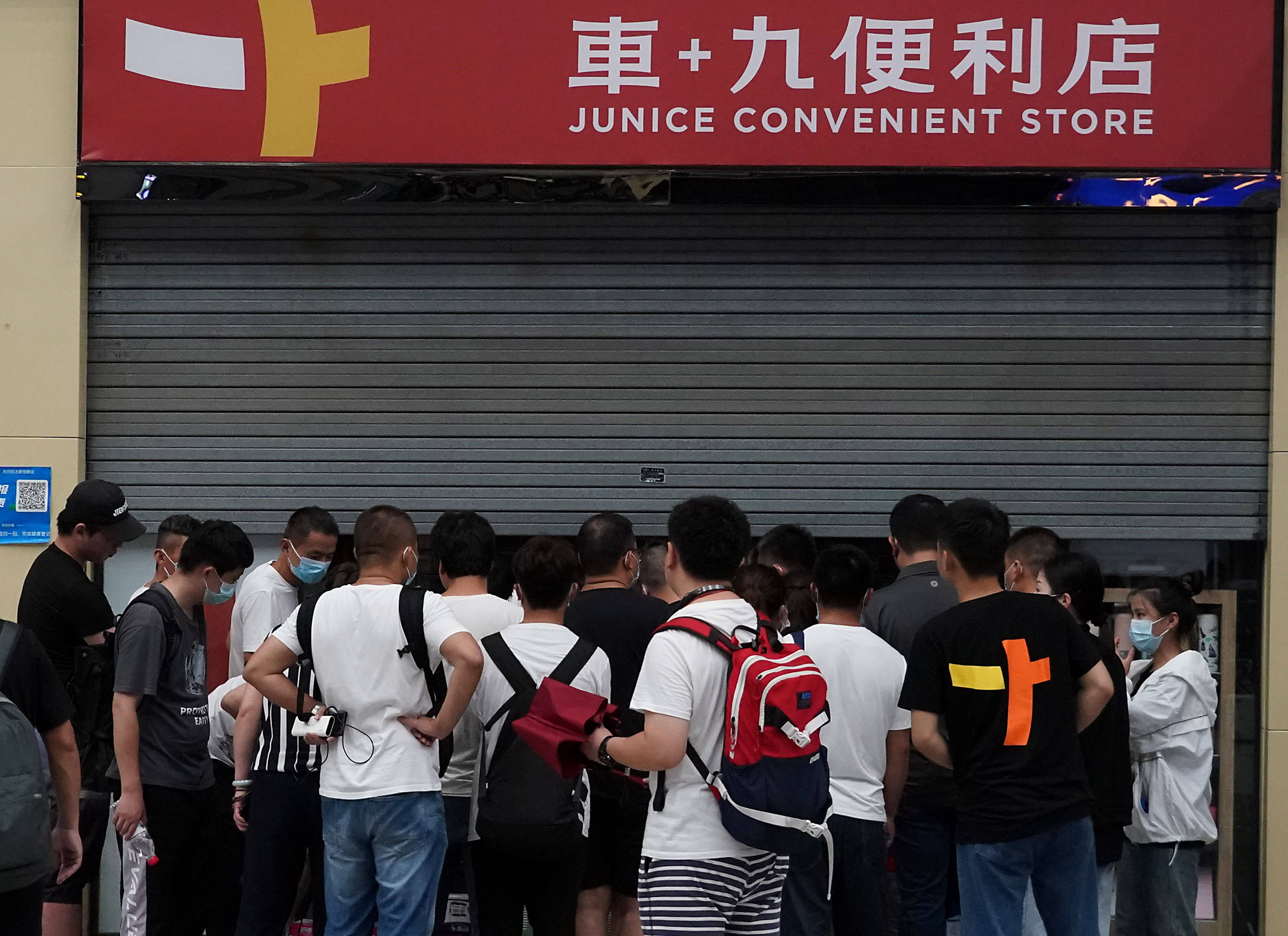 7月20日,滞留旅客在郑州东站一家便利店外排队购物