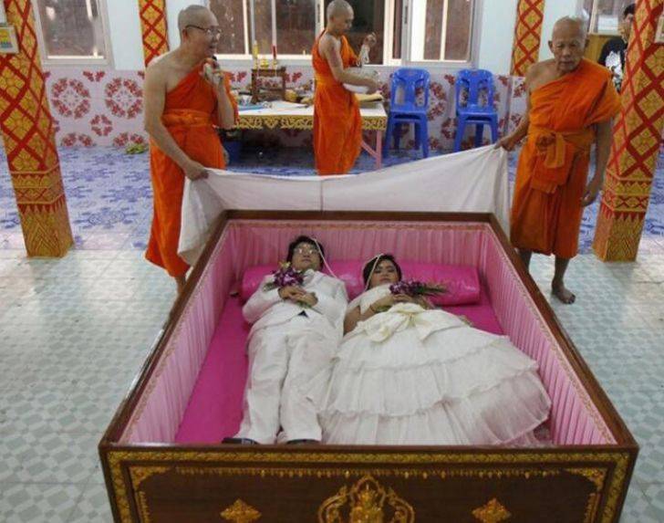 泰国一对新婚夫妻躺在棺材里,一旁的僧人在为他们祈福.