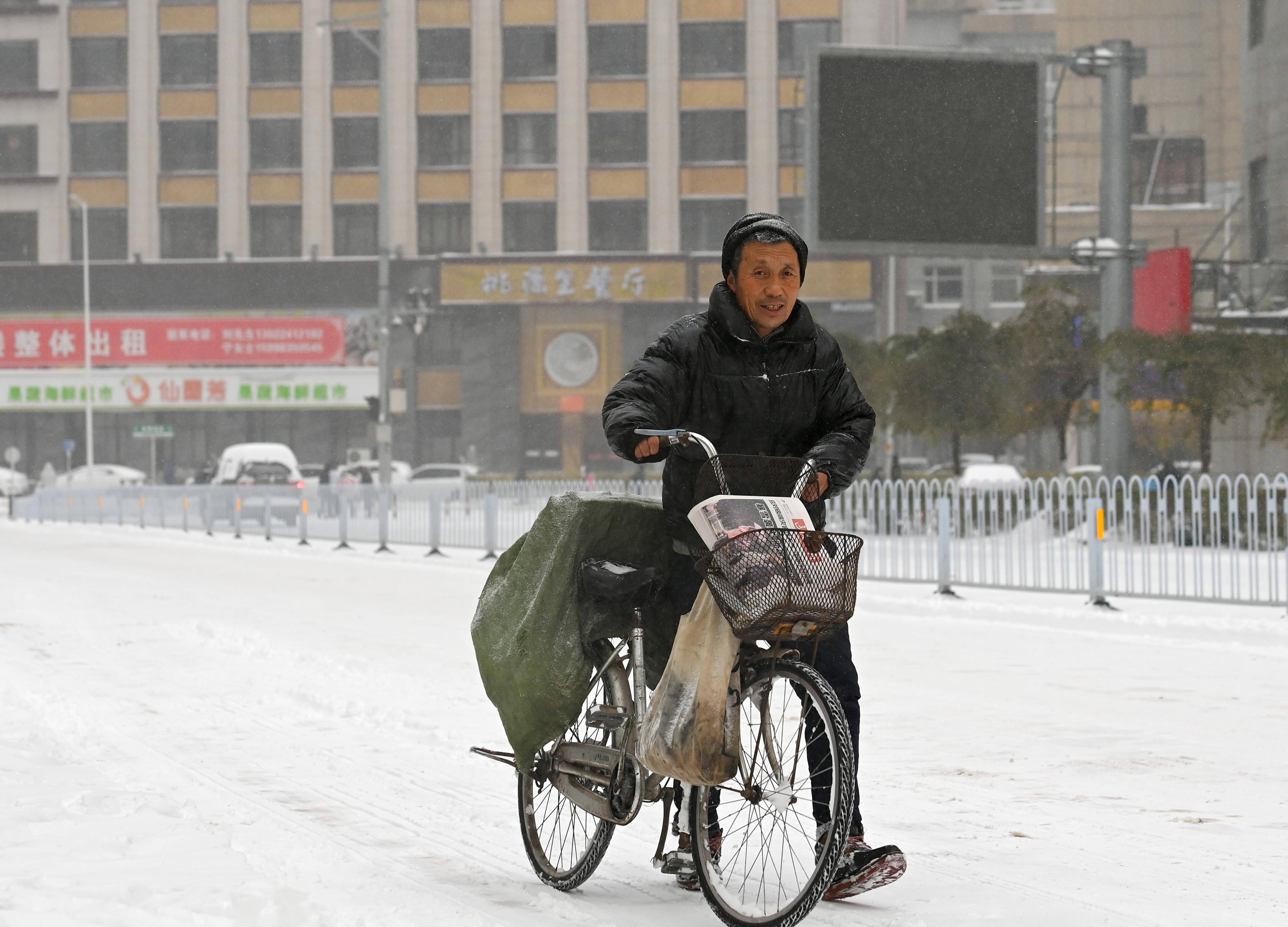 11月8日,在沈阳市沈河区,一名邮递员在雪中送报