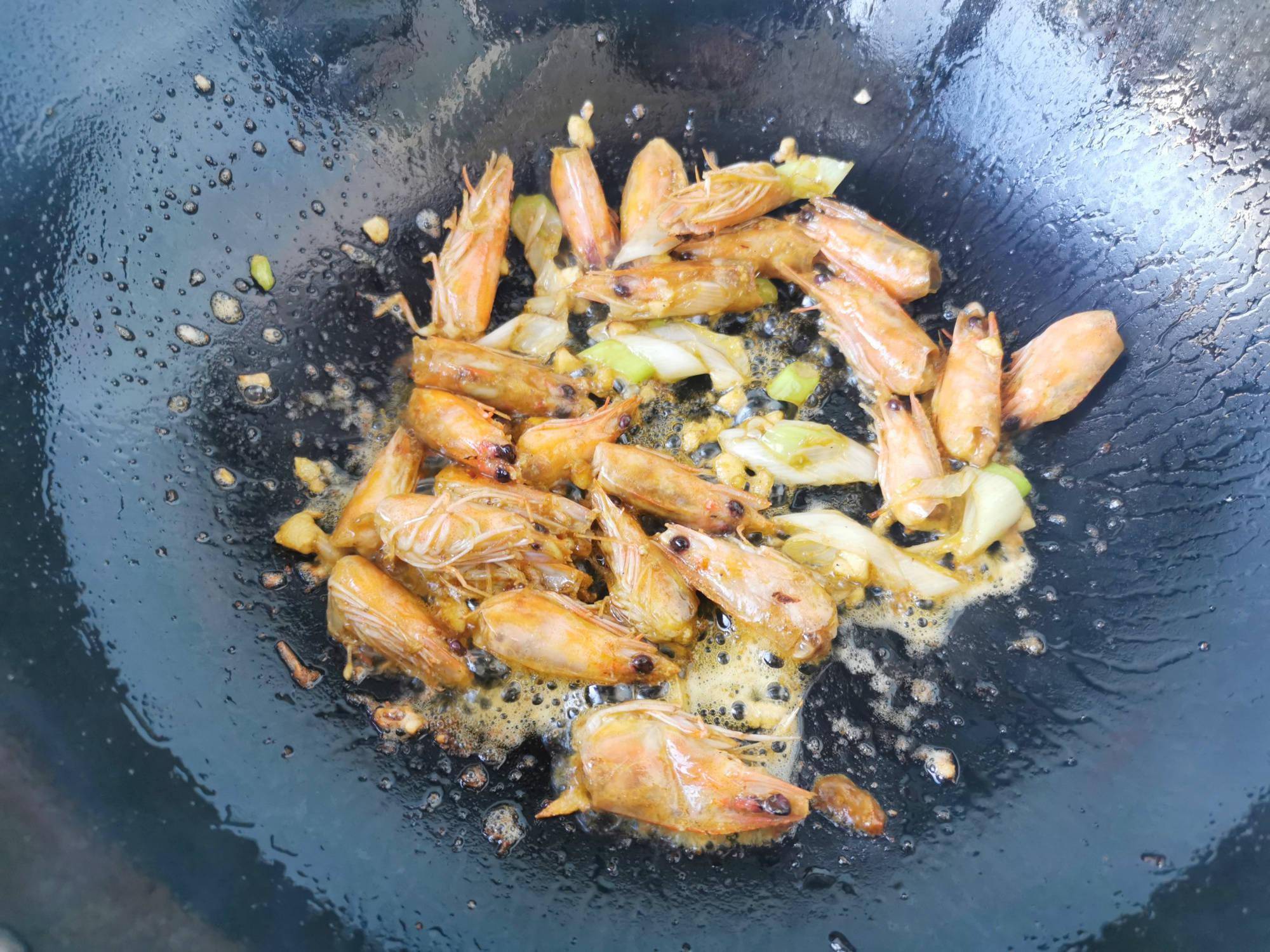 4,锅中倒入食用油,爆香葱蒜,倒入虾头煸炒,一直将虾头煸炒出红油为止.