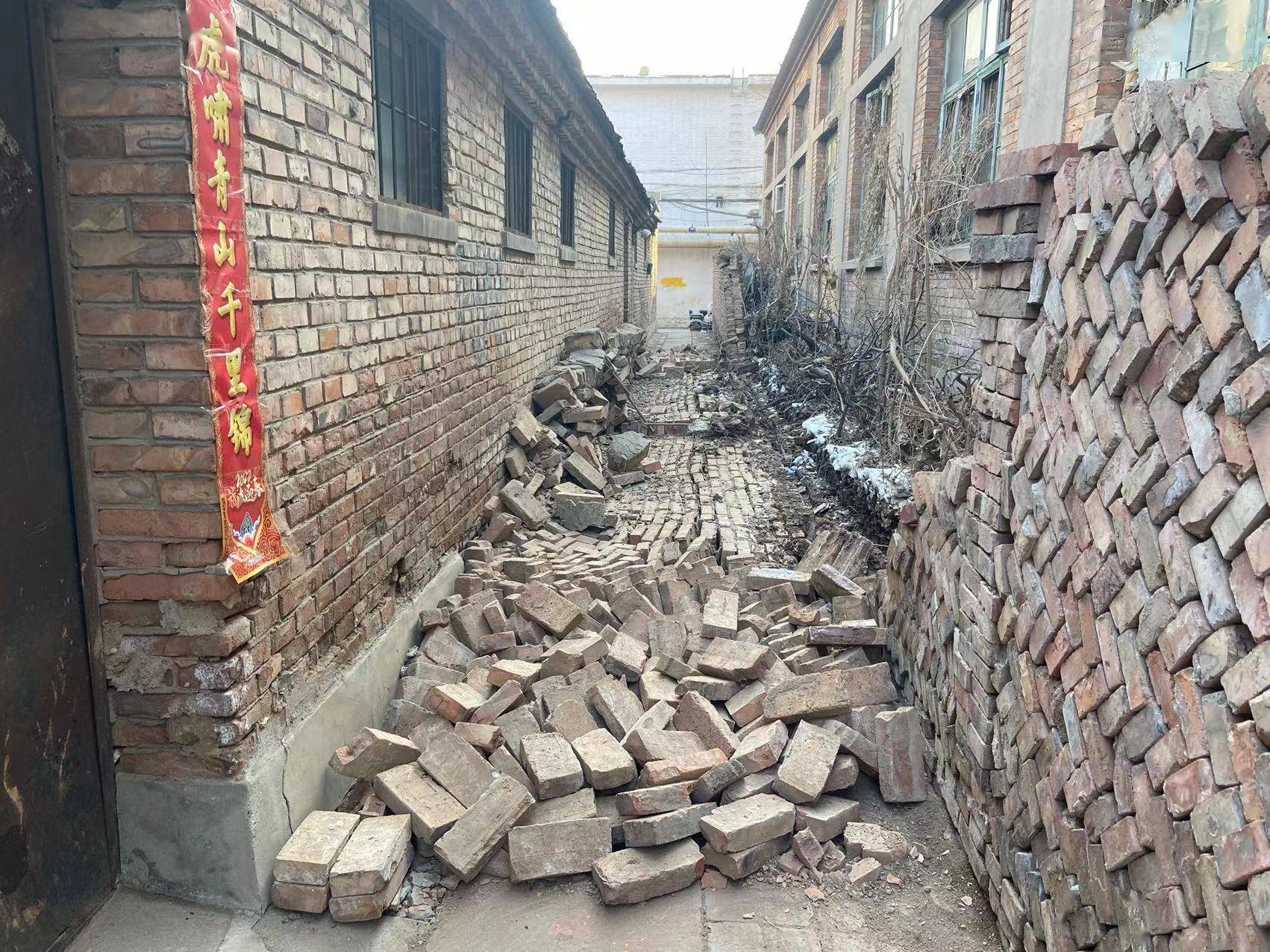只见约50米长的狭窄胡同中间,十几米长的墙体齐根断裂,凌乱的砖块铺满