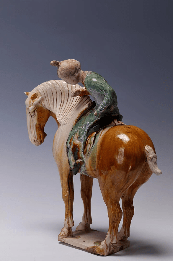 三彩双丫髻女骑马俑 颈部以下身施黄釉、绿釉、筌蹄施黄釉,裙下鞋尖外露。高28厘米。